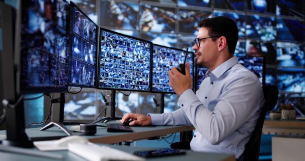 Security operations manager holding walkie talkie while observing wall monitor array